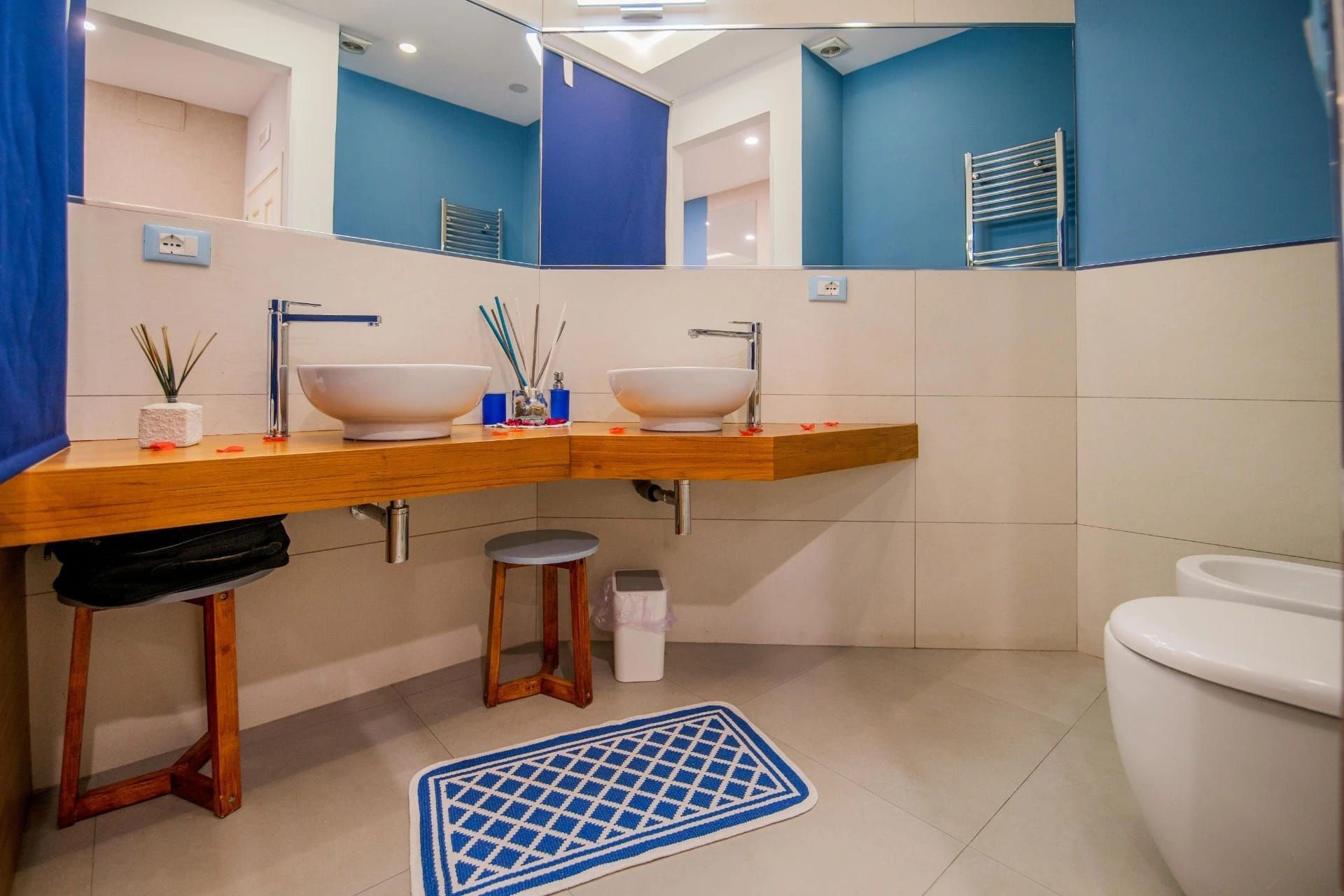 Bagno moderno con doppio lavabo, pareti blu, piano in legno, specchio e WC.