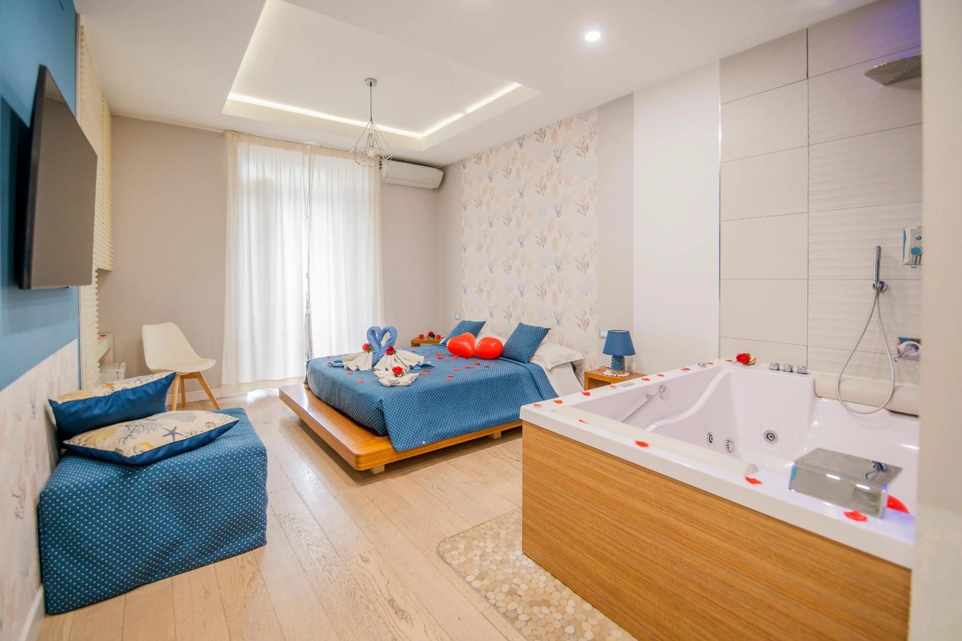 Luminosa camera da letto moderna con biancheria da letto blu, chaise longue e vasca da bagno bianca accanto al letto.