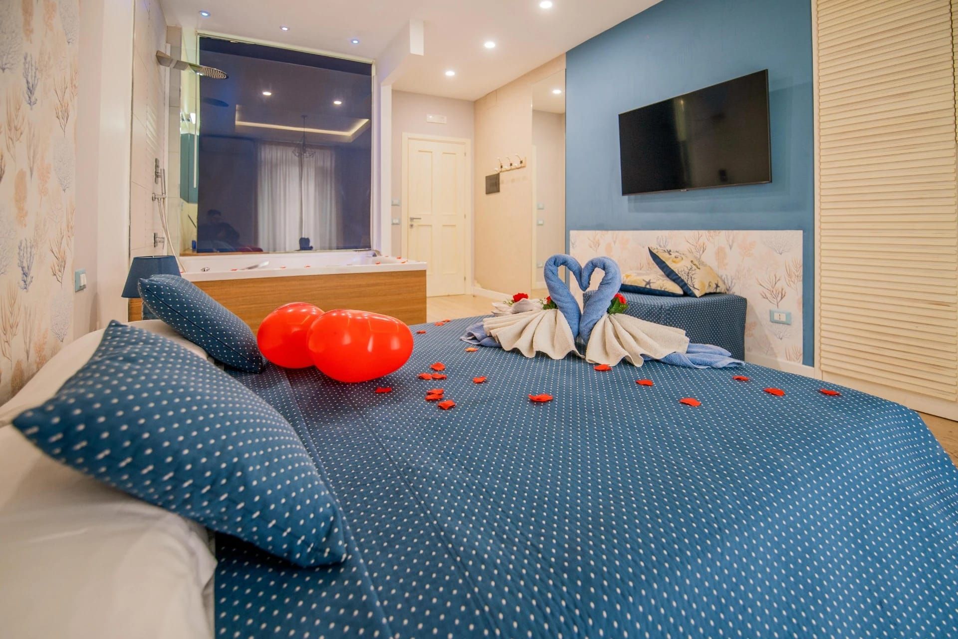 Letto a pois blu con palloncini rossi e cigni di asciugamani in una luminosa camera da letto moderna
