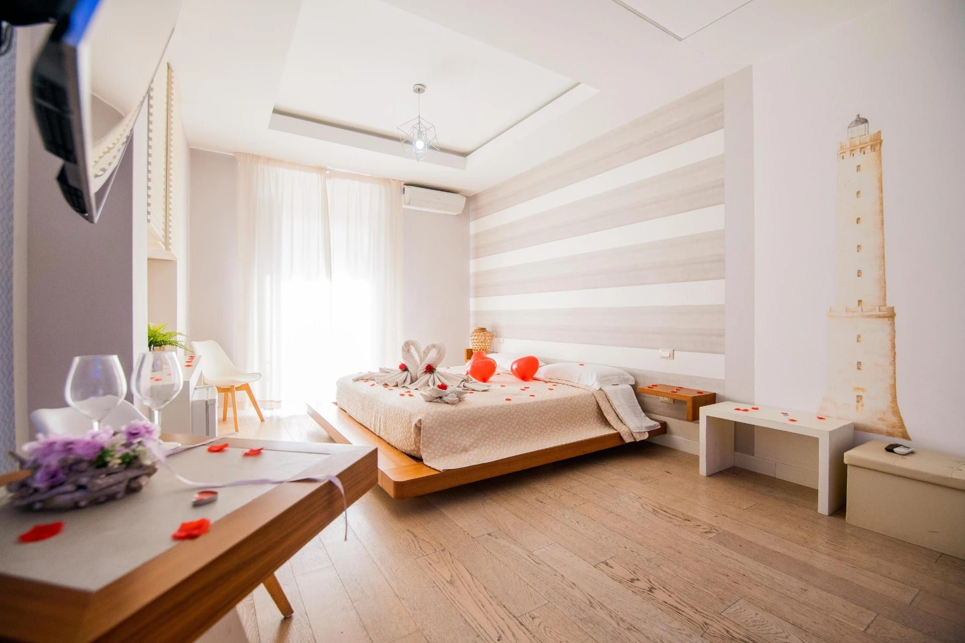 Camera da letto luminosa e ariosa con letto basso in legno, parete decorativa a righe, ampie finestre e mobili bianchi.