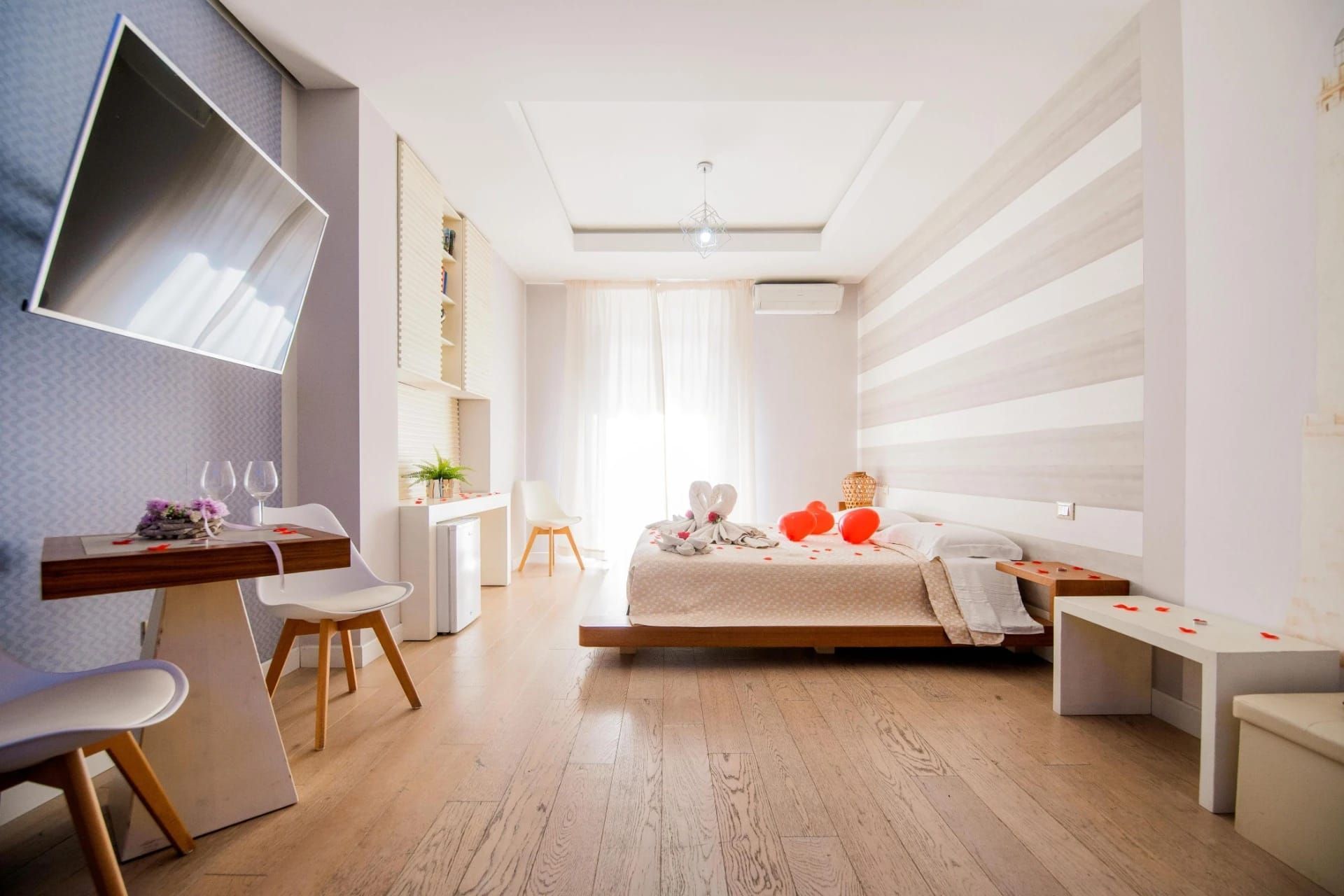 Camera da letto luminosa e minimalista con letto, scrivania, sedia e decorazione murale a righe.