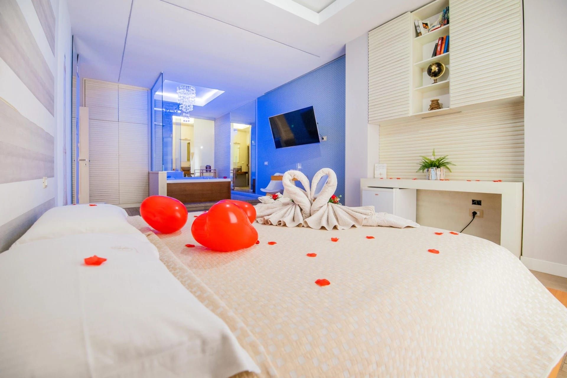 Camera d'albergo moderna con letto decorato con petali rossi e palloncini, e cigni di asciugamani sul letto