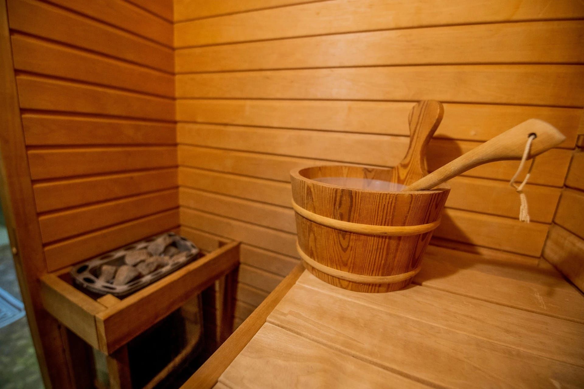 Sauna rivestita in legno con secchio e mestolo in legno accanto a una stufa riempita di pietre.