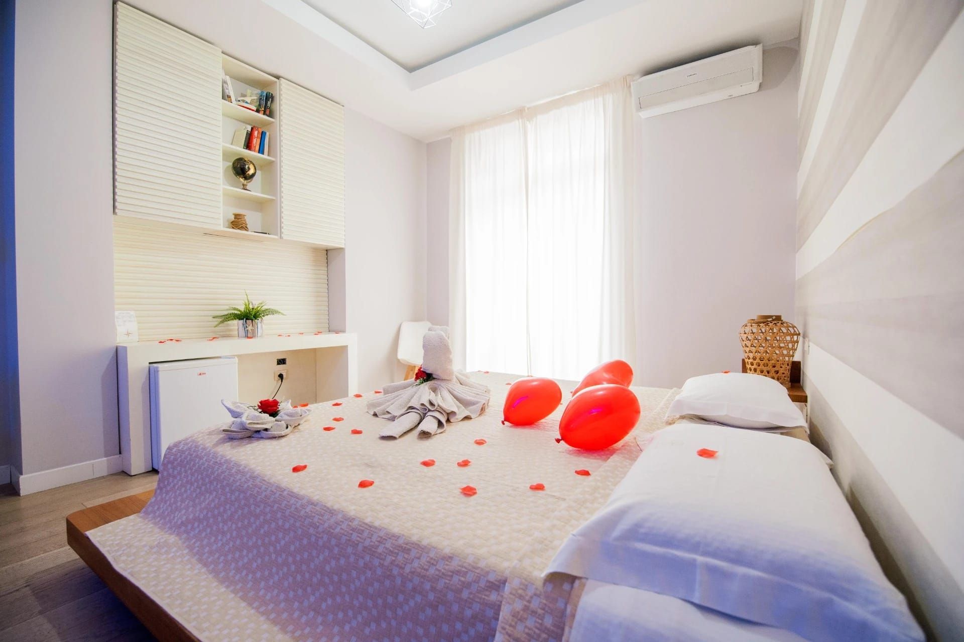 Luminosa camera da letto moderna con letto, cuscini a forma di cuore rosso e morbida luce naturale proveniente da una finestra.