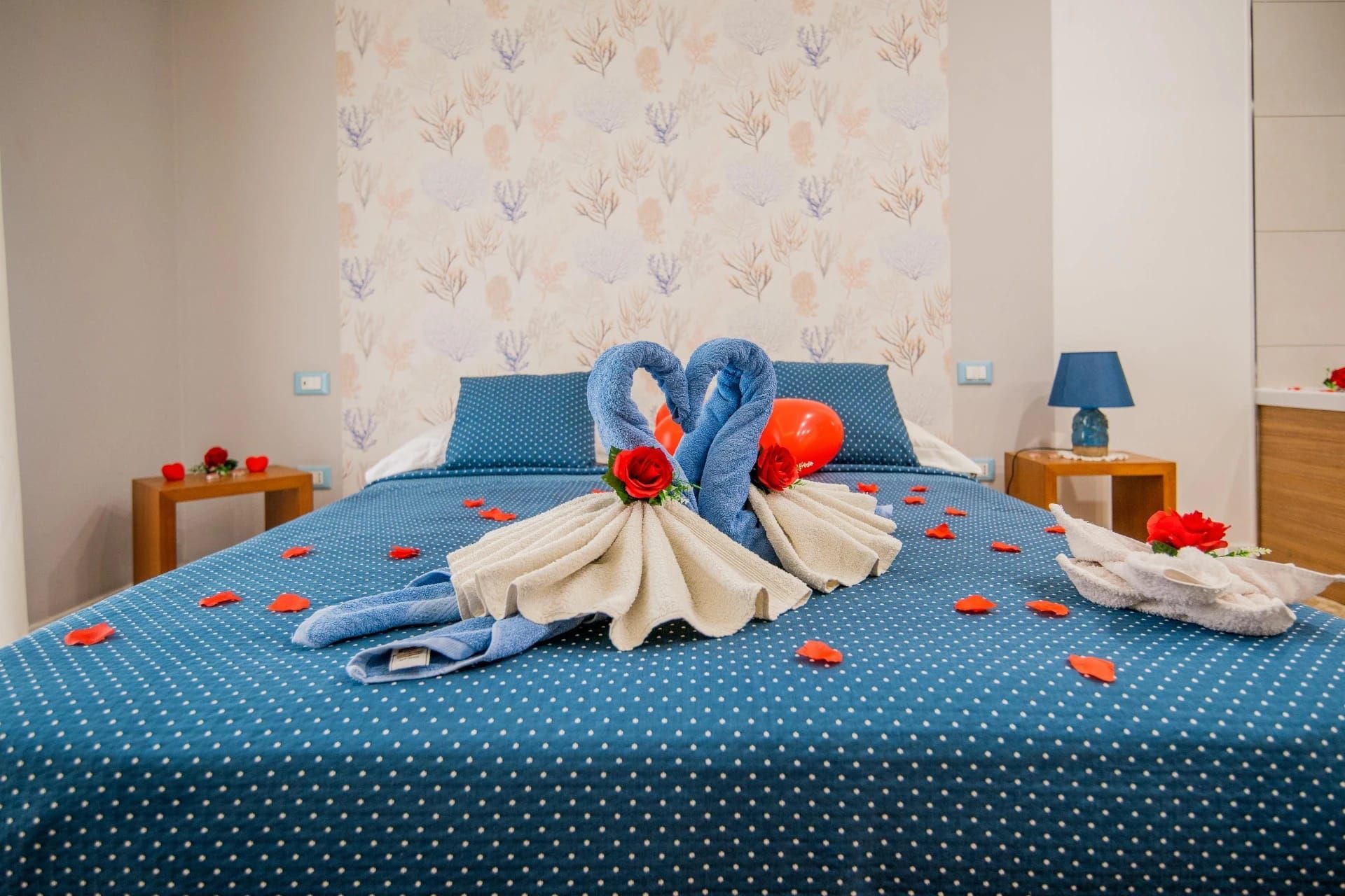 Camera da letto con copriletto a pois blu, cigni di asciugamani e petali di rose rosse sparsi sul letto.