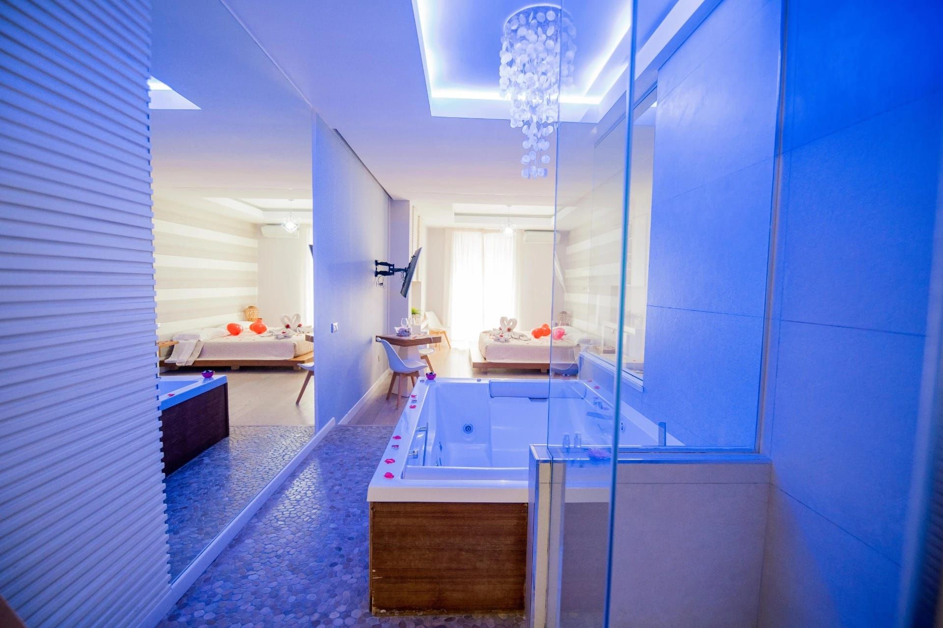 Bagno moderno illuminato di blu con vasca freestanding, doccia in vetro e zona relax adiacente.
