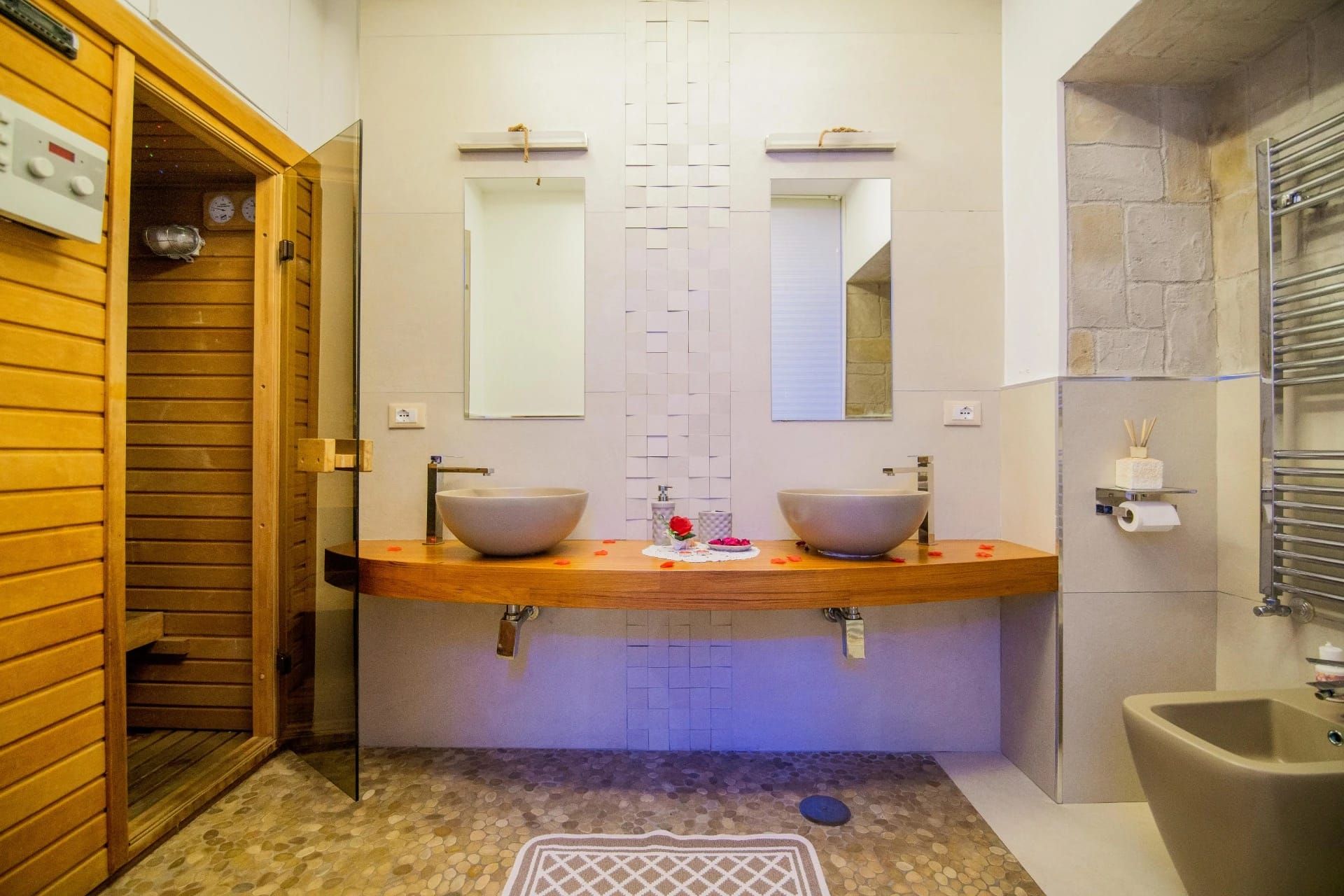 Bagno in stile spa con due lavabi a ciotola, specchi, piano in legno, porta per sauna e zona doccia.
