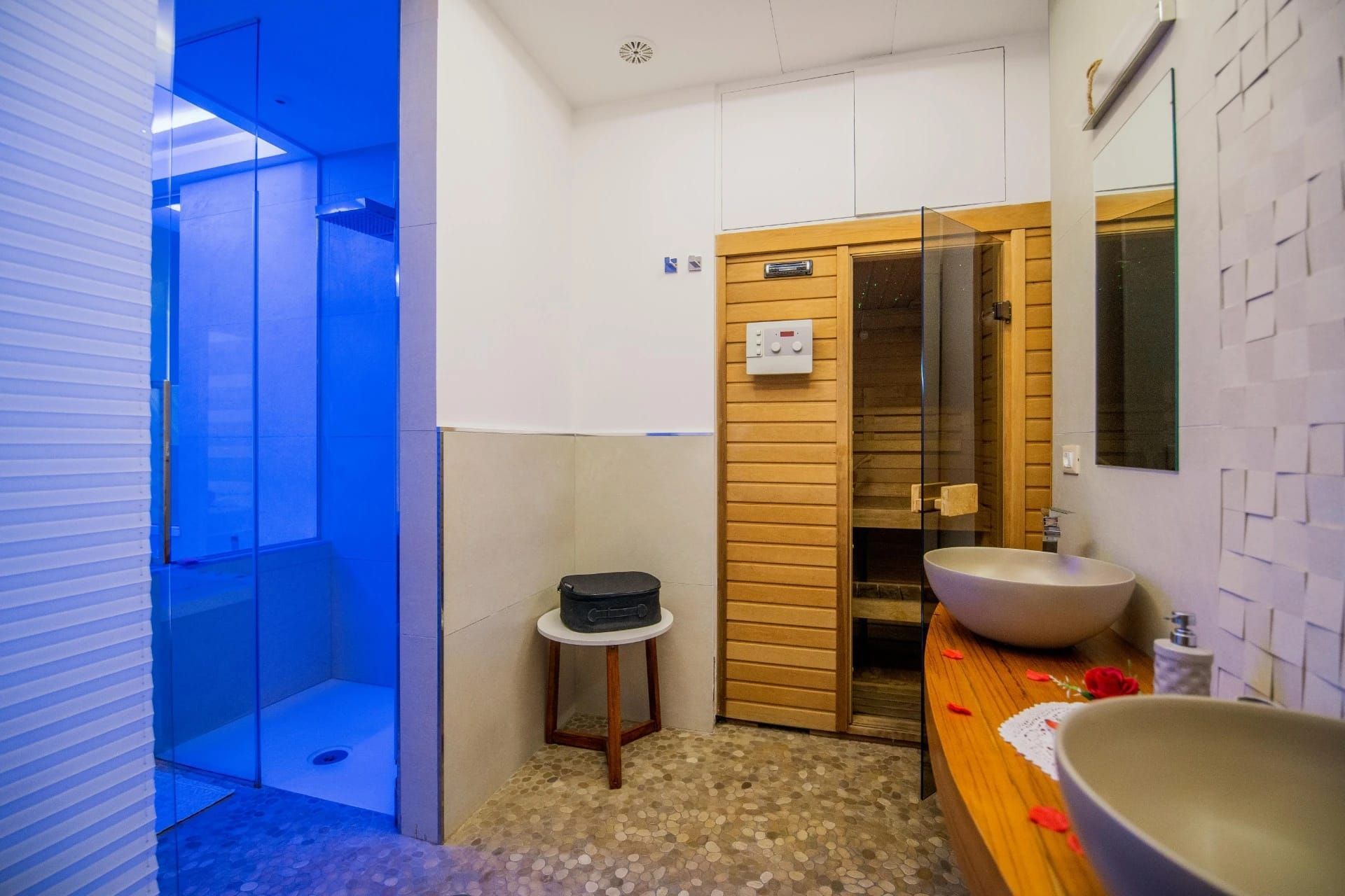 Bagno moderno con box doccia con luci blu, sauna in legno e lavabo.