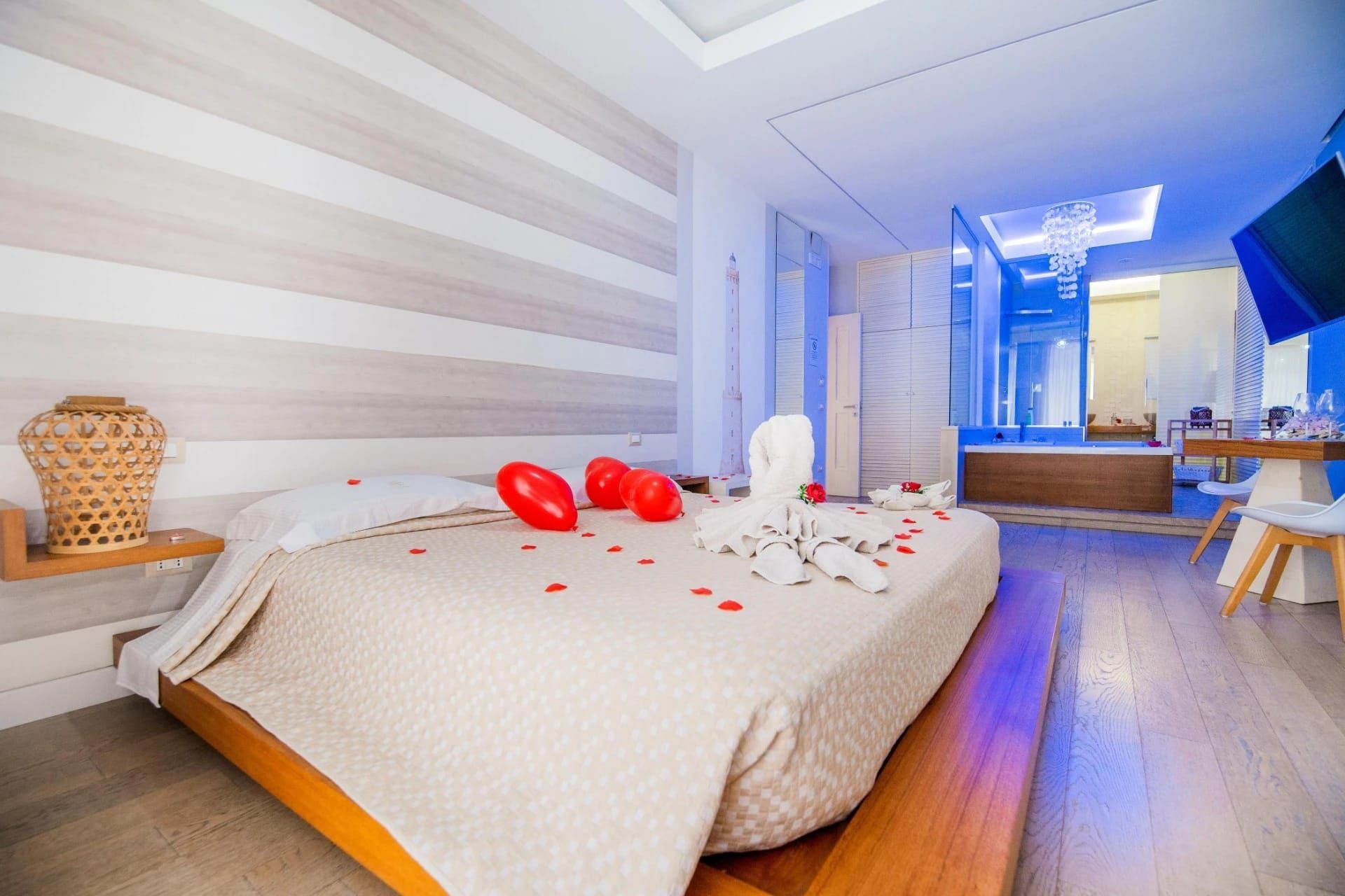 Camera da letto romantica con letto, palloncini a forma di cuore rossi e petali di rosa in un interno luminoso e moderno.