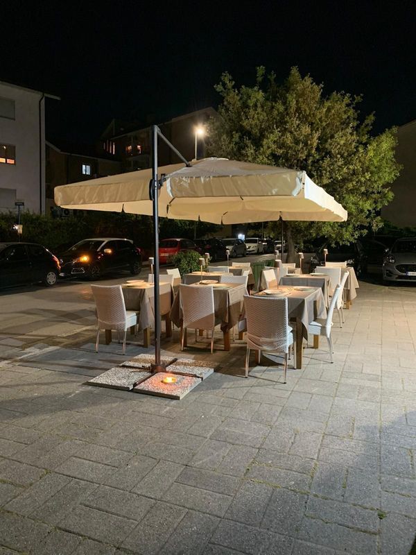 Di sera, il ristorante dispone di tavoli all'aperto sotto grandi ombrelloni beige, con tavoli e sedie su una terrazza pavimentata.