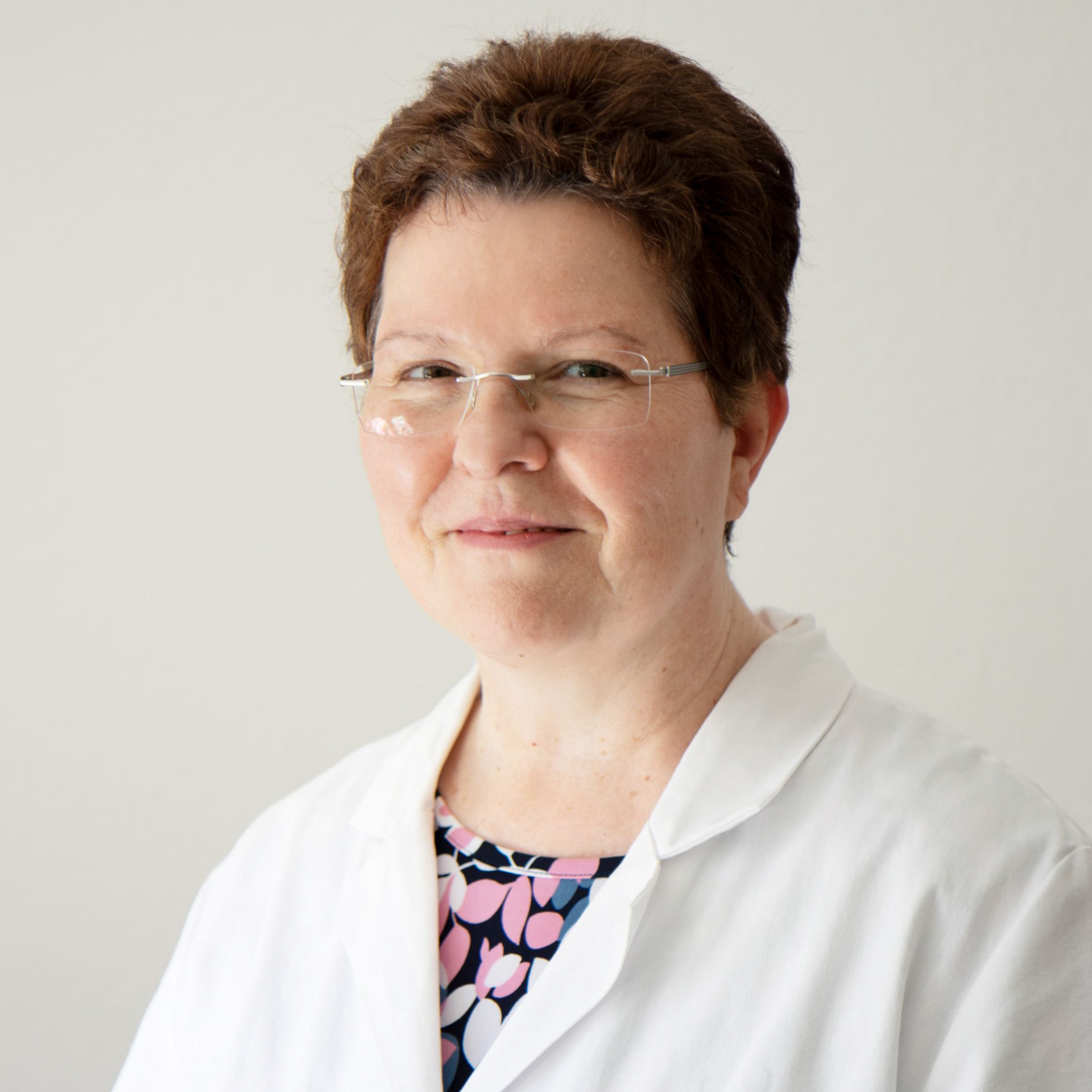 Frau im Laborkittel und mit Brille lächelt; heller Hintergrund.