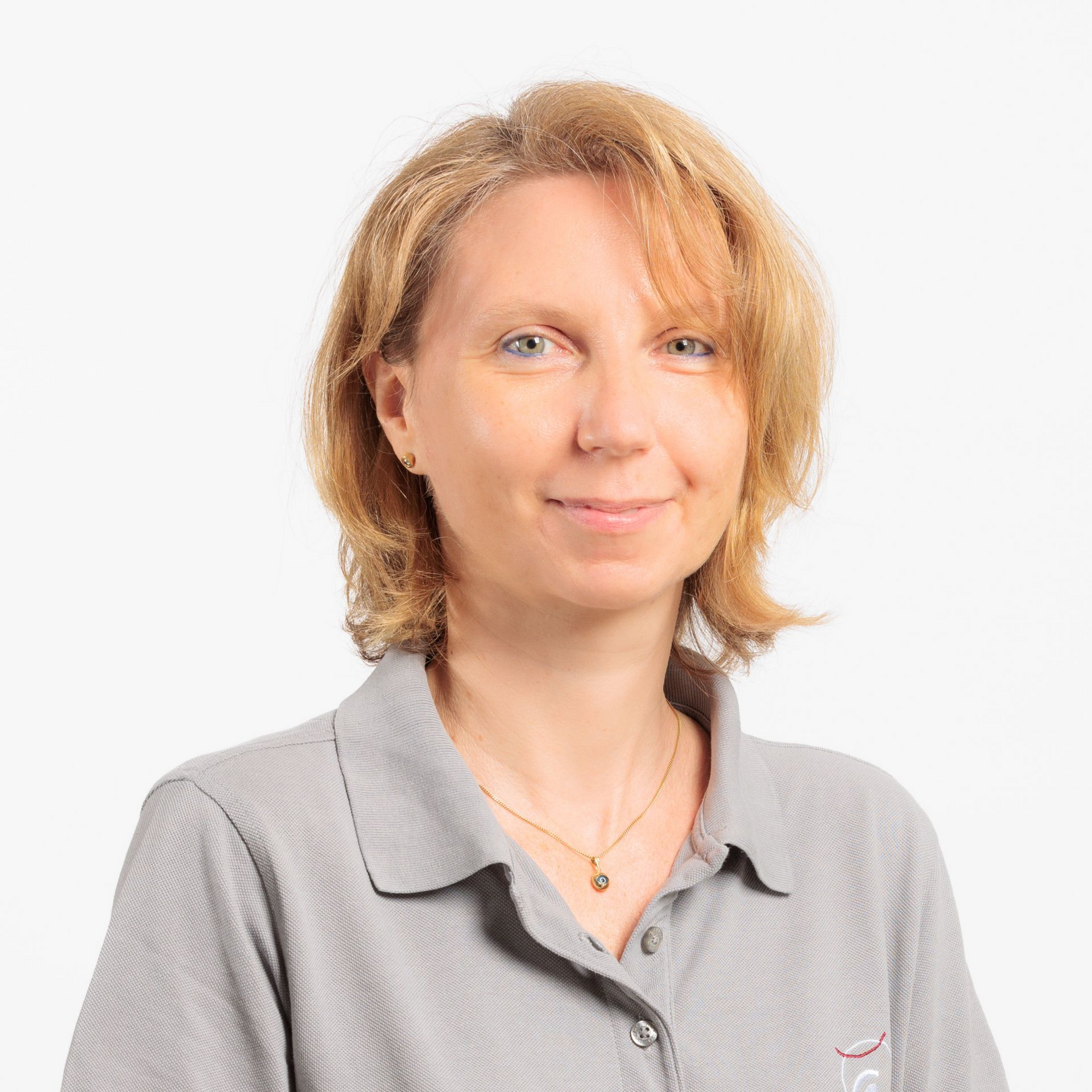 Frau mit blonden Haaren, die ein graues Poloshirt trägt, lächelt vor einem weißen Hintergrund.