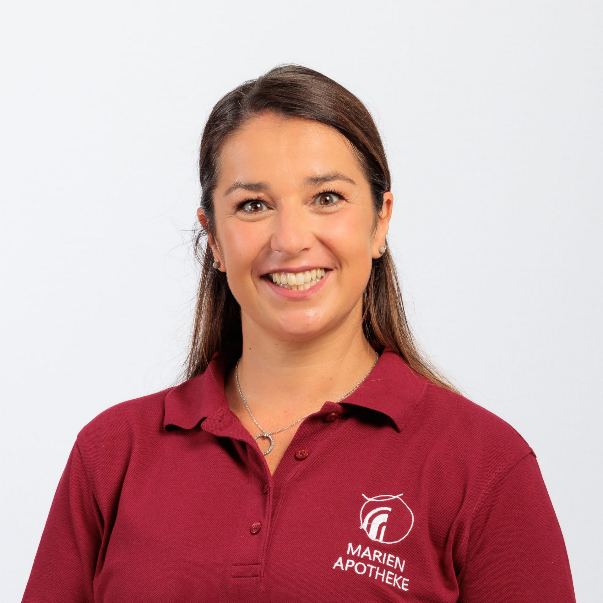 Frau in einem roten Poloshirt mit dem Logo „Marien Apotheke“, lächelnd, Studioaufnahme.