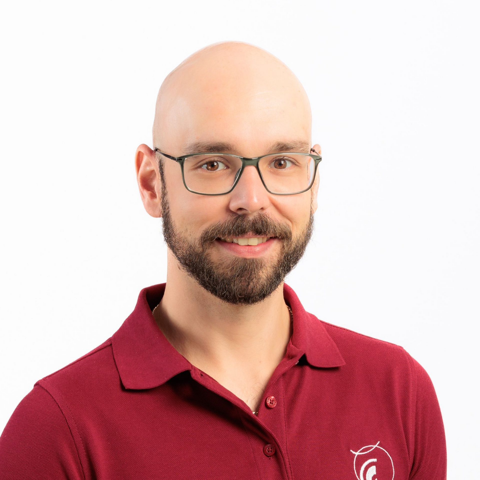 Ein kahlköpfiger Mann mit Bart, Brille und kastanienbraunem Poloshirt