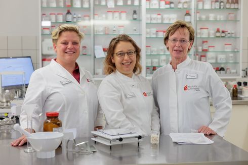 Drei Apothekerinnen posieren in einer Apotheke für ein Foto.