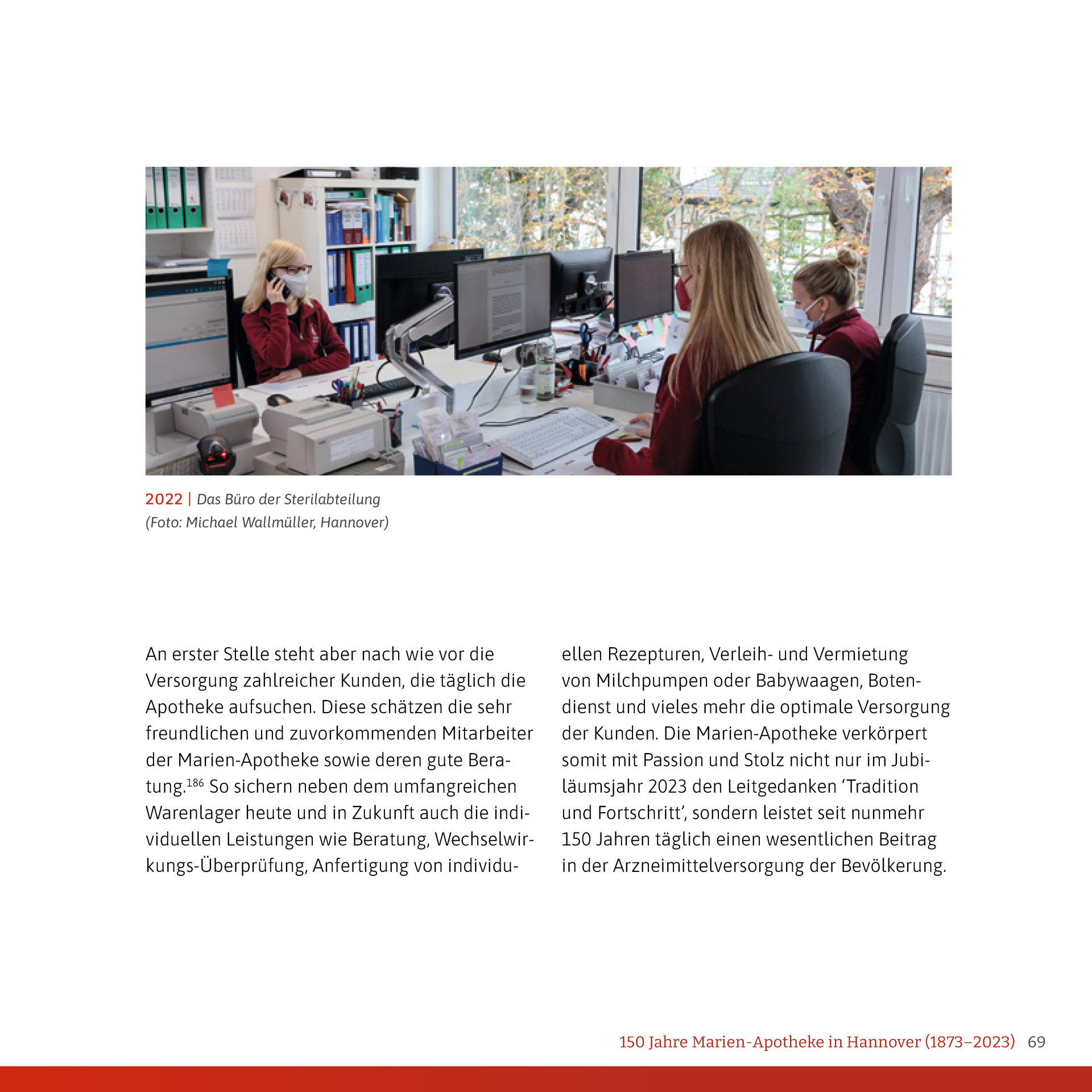Eine Frau sitzt an einem Schreibtisch vor einem Computer und telefoniert mit einem Mobiltelefon.