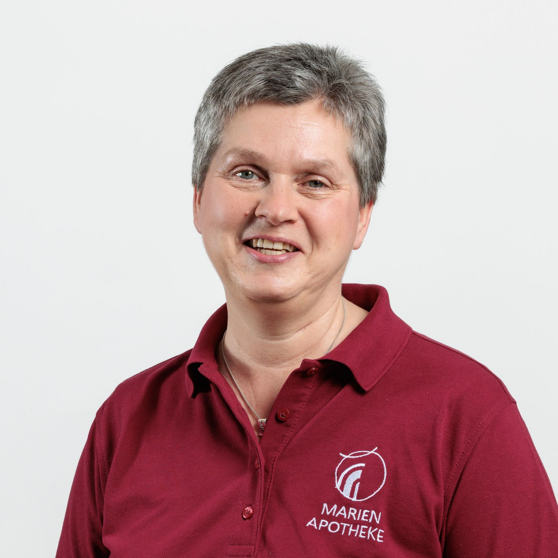 Eine Frau in einem weinroten Hemd mit dem Logo „Marien Apotheke“ lächelt in die Kamera.