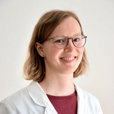 Eine Frau mit Brille und weißem Kittel lächelt in die Kamera.