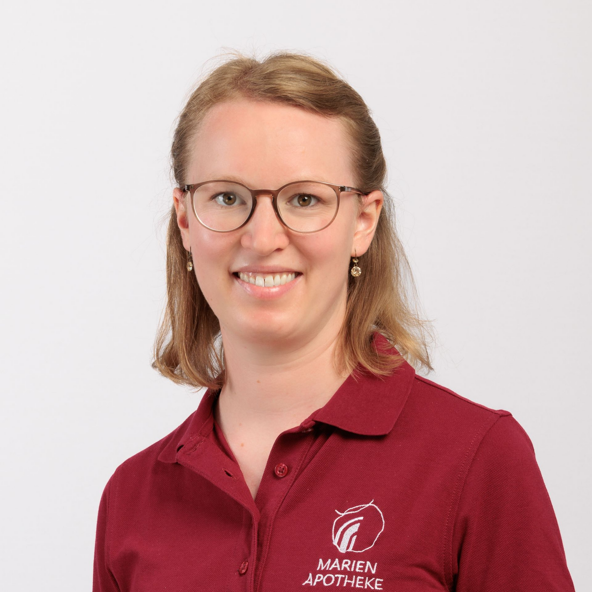 Frau mit Brille und weinrotem Hemd lächelt, Logo „Marien Apotheke“