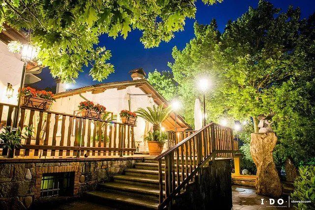 Esterno del ristorante di notte con scale, ringhiere in legno e alberi illuminati.
