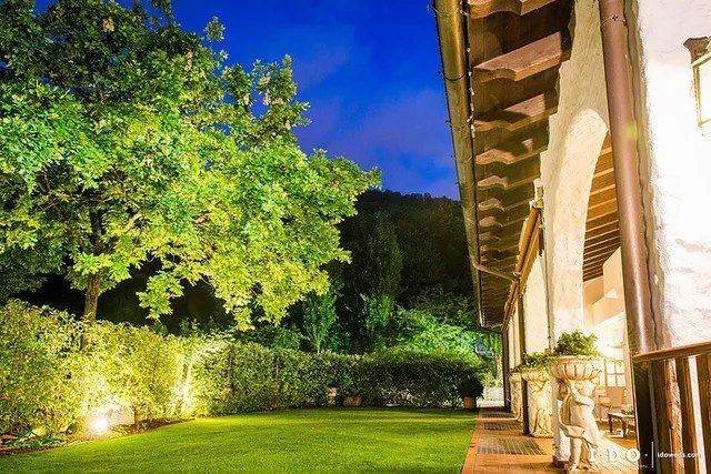 Un prato verde lussureggiante e alberi illuminati al tramonto accanto a un edificio con un passaggio coperto.