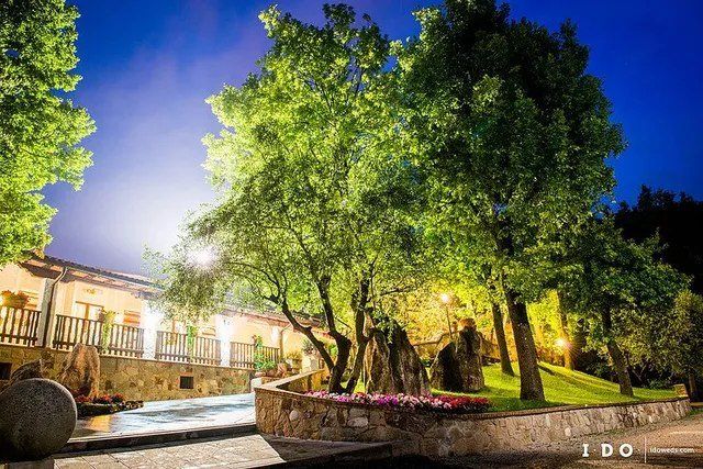 Scena notturna: alberi e un edificio illuminati lungo un ruscello, con un cielo blu scuro.