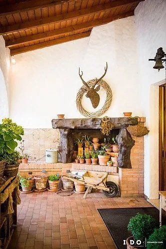Area esterna rustica con camino, piante e decorazione a forma di testa di cervo.