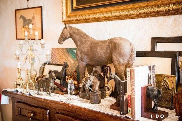 Una collezione di statuette di cavalli su uno scaffale di legno, con opere d'arte e un candelabro.