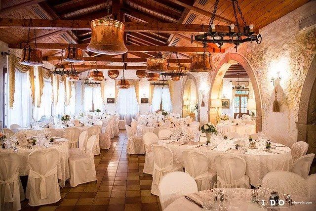 Elegante ricevimento di nozze: tavoli apparecchiati con tovaglie bianche, porte ad arco, luci calde, soffitto in legno.
