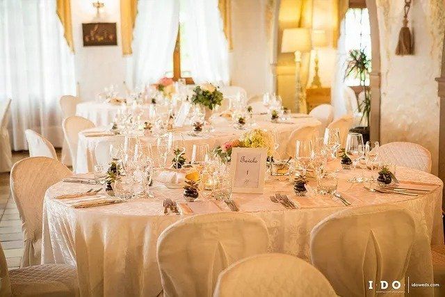 Eleganti tavoli da pranzo apparecchiati per un ricevimento di nozze in una sala illuminata in modo caldo.