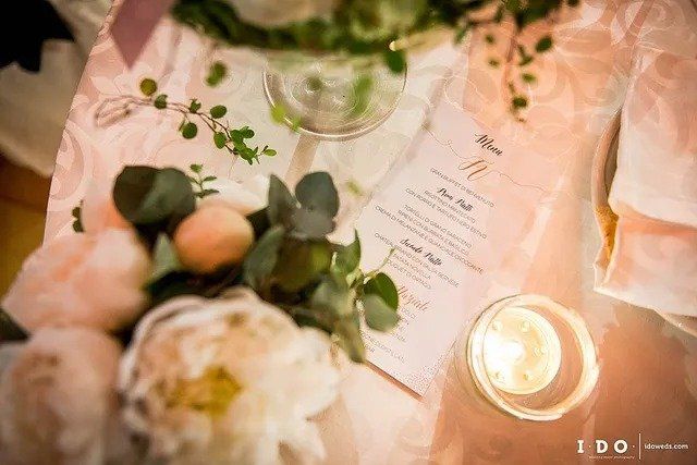 Apparecchiatura del tavolo con menù, fiori e candela accesa. Illuminazione rosa tenue, dettagli eleganti.