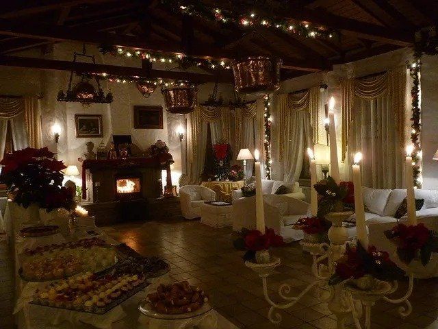 Soggiorno festoso con camino, divani bianchi, candele accese e un tavolo da buffet, decorato per Natale.