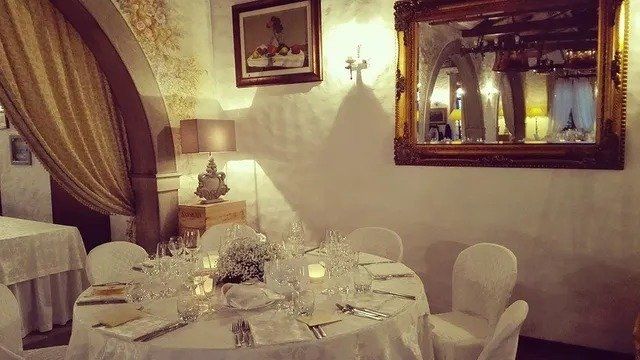 Elegante tavolo da pranzo apparecchiato per un pasto in un ristorante con sedie bianche e uno specchio dorato.