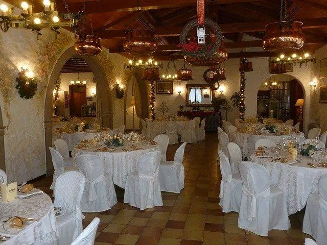 Sala da pranzo del ristorante con tavoli rotondi, tovaglie bianche e sedie decorate. Lampadari in rame.