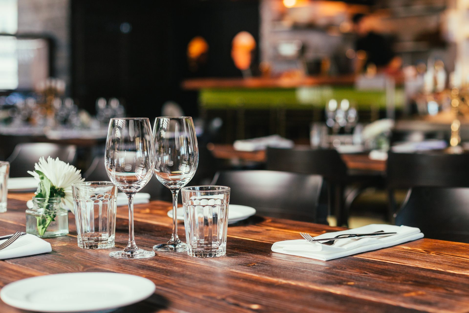 Tavolo da ristorante apparecchiato per cenare con bicchieri da vino, bicchieri da acqua e piatti bianchi.