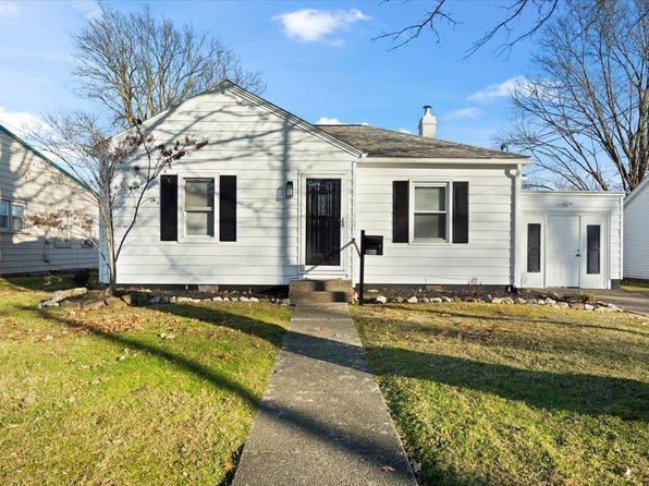 A white house with black shutters and a sidewalk in front of it.