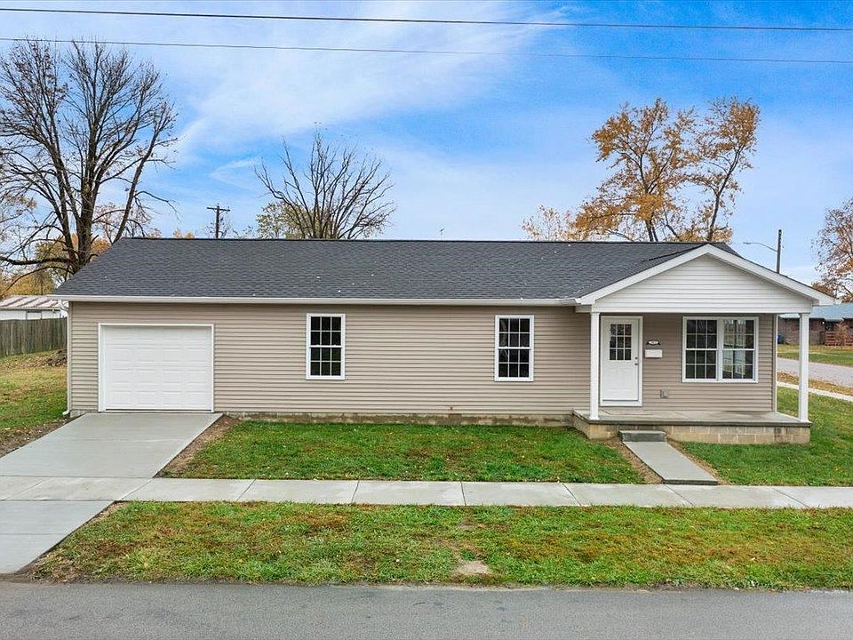 A small house with a garage and a sidewalk in front of it.