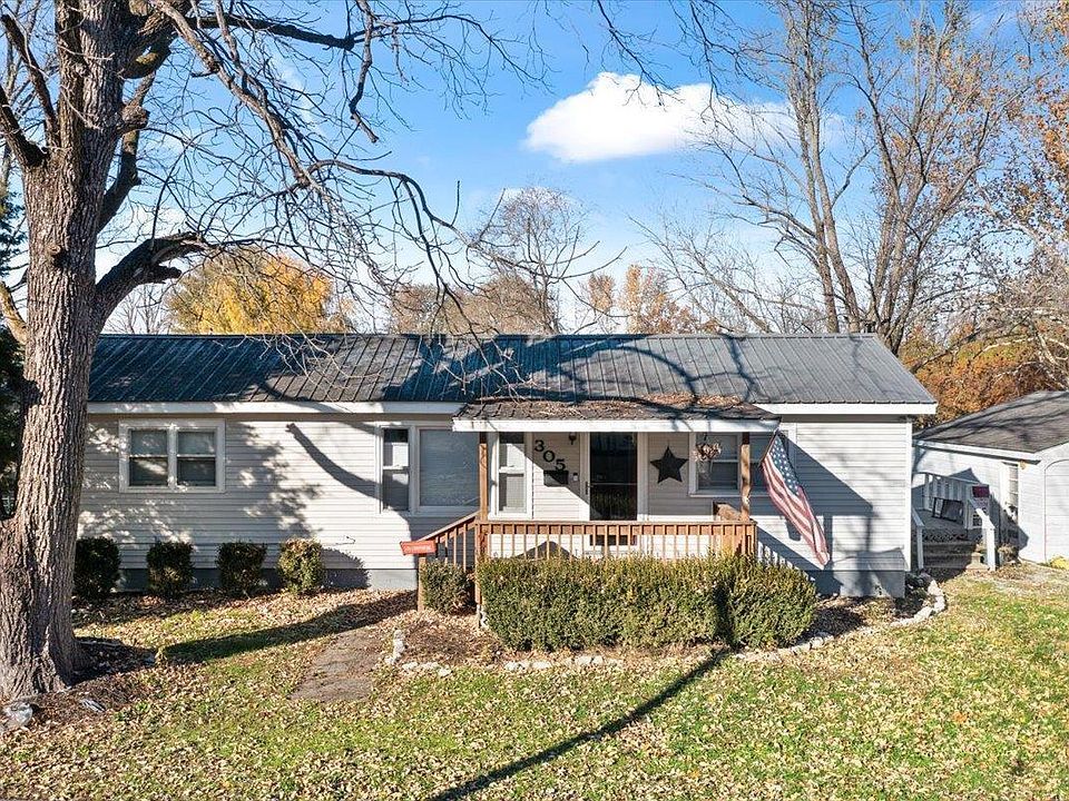 A small house with a porch and a tree in front of it.