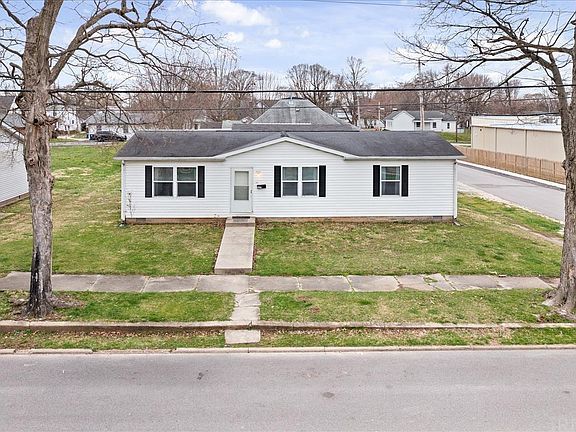 A small white house with black shutters is sitting on top of a lush green lawn.