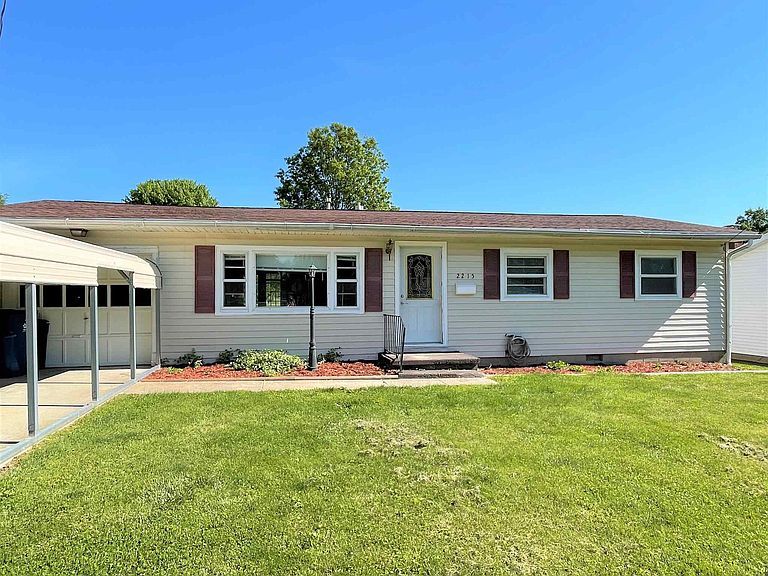 A white house with brown shutters and a carport in front of it.