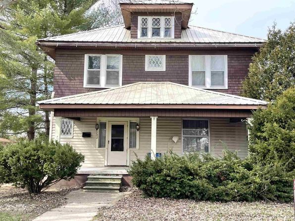 A large house with a metal roof is surrounded by trees and bushes.