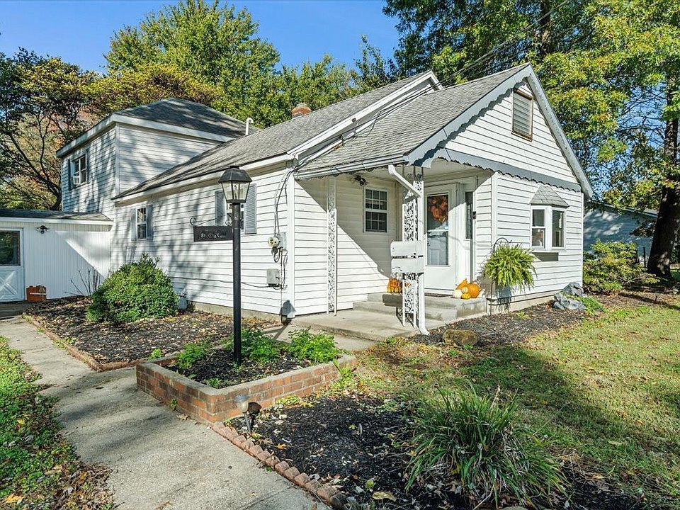 A small white house with a porch and a brick walkway in front of it.
