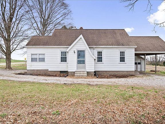 A small white house with a brown roof is sitting in the middle of a field.