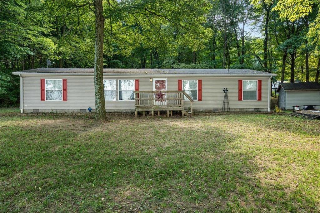 A mobile home with red shutters is sitting in the middle of a lush green field.