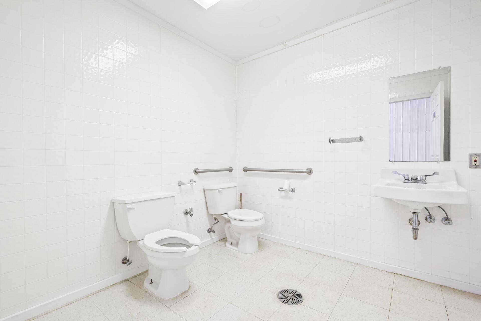 A bathroom with two toilets , a sink and a mirror.