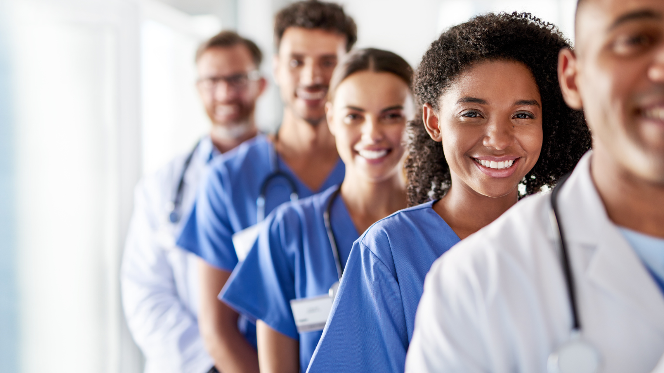 A group of doctors and nurses are standing in a row and smiling.