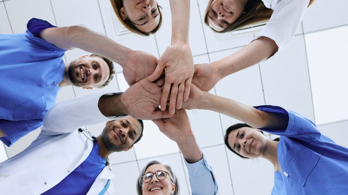 A group of doctors and nurses are putting their hands together in a circle.