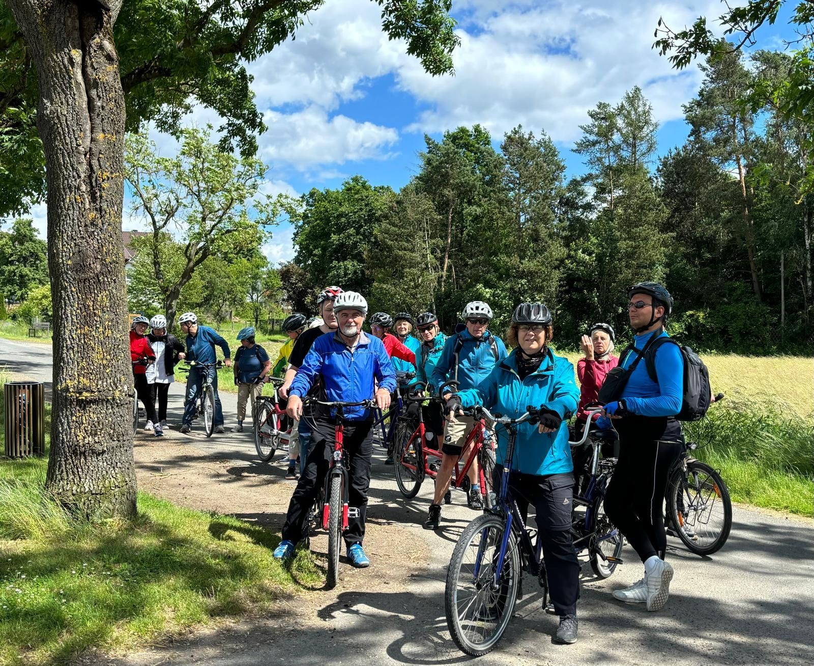 Gruppe von 15 Radfahrern in wetterfester Kleidung und Helmen in ländlicher Umgebung.