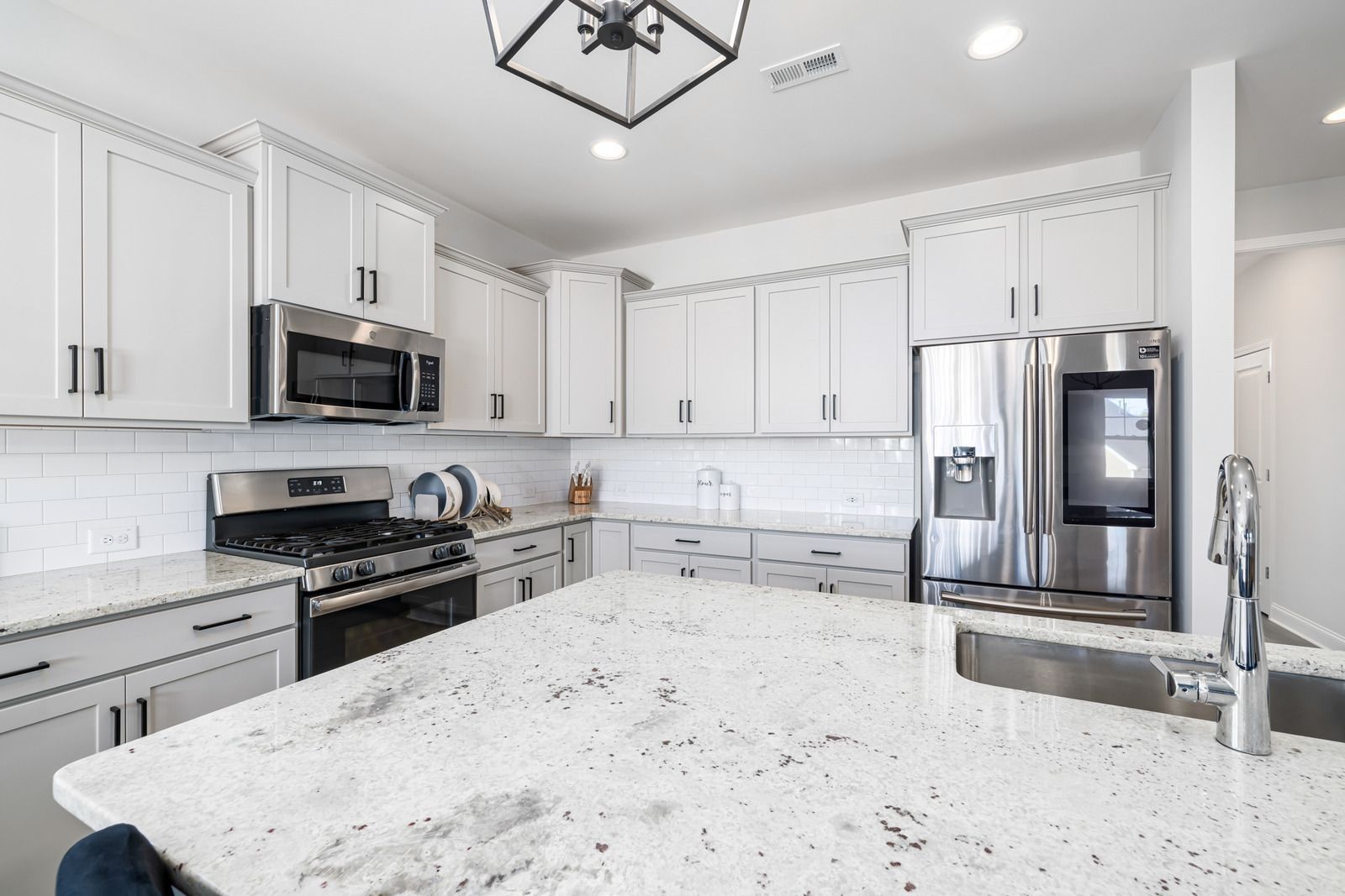 Bright modern kitchen with white cabinets, stainless appliances, and a large granite island.