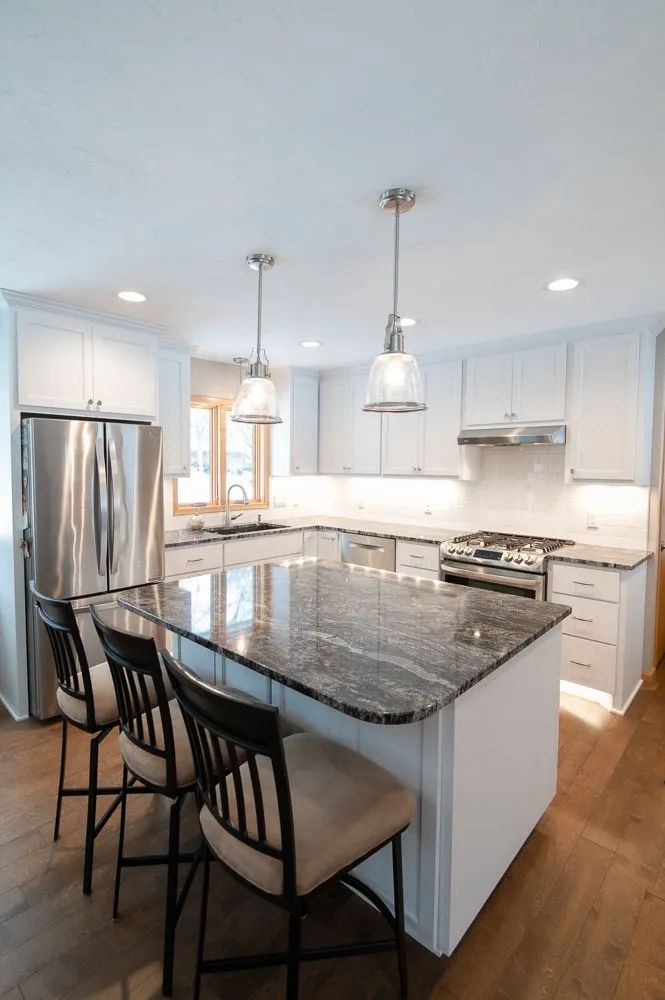 Modern white kitchen with granite island, stainless steel appliances, and bar stools